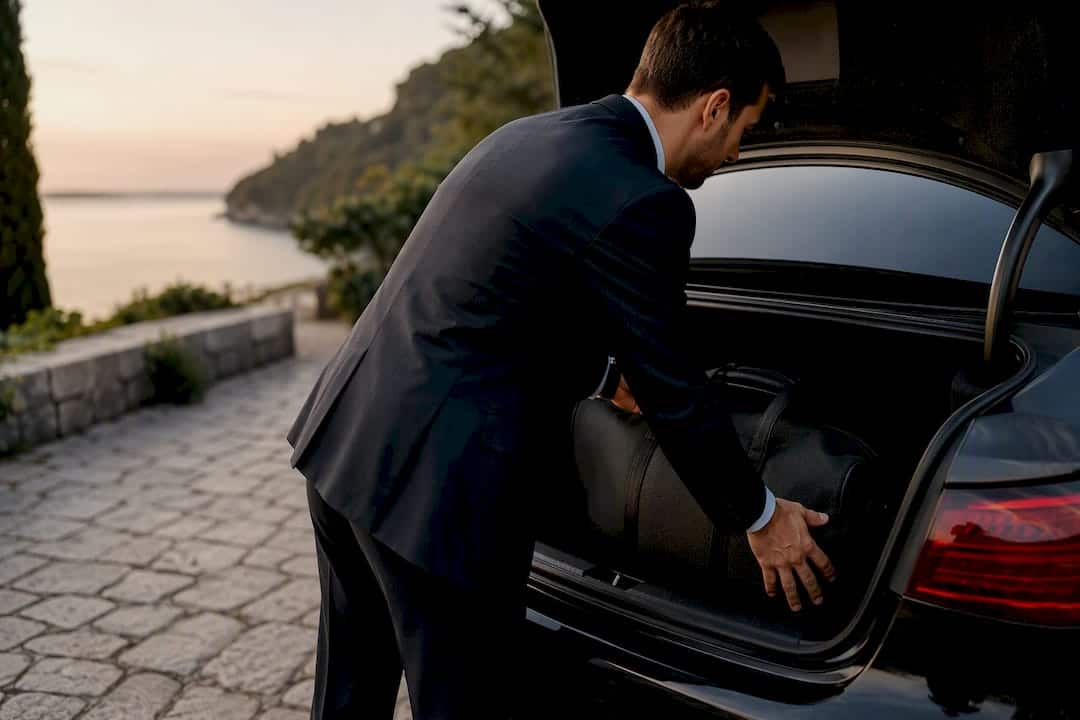 Chauffeur loading luggage into plain vehicle trunk